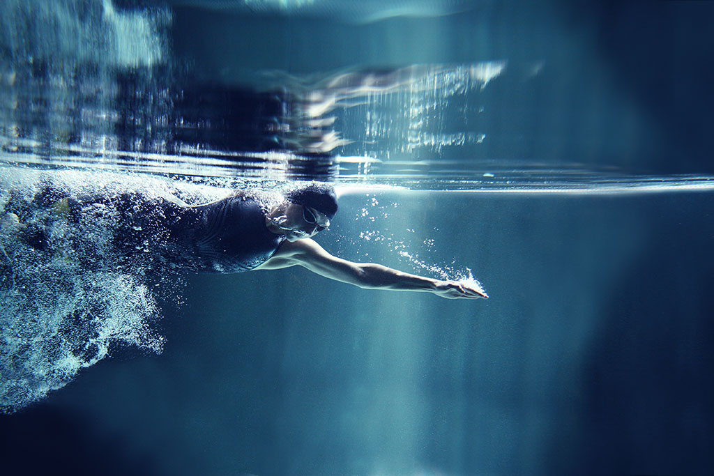 Athlete swimming freestyle on blue background, underwater view